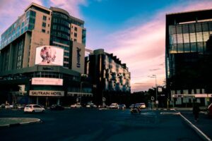 A bustling city street with modern skyscrapers and vehicles at sunset, Gautrain Hotel visible.