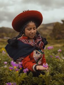 A young Peruvian woman in traditional clothing admires flowers in a Cusco field.
