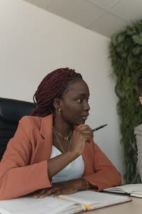 Confident African American woman in corporate attire with pen and notebook in an office environment.