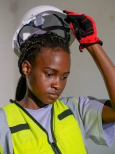 Focused African American female engineer adjusting her hardhat with safety gear on site.