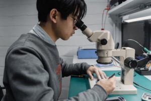 Young male technician working with a microscope in a laboratory setting, focused on electronics.