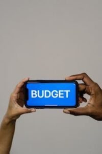 Hands holding a smartphone displaying the word 'BUDGET',' illustrating a financial concept.